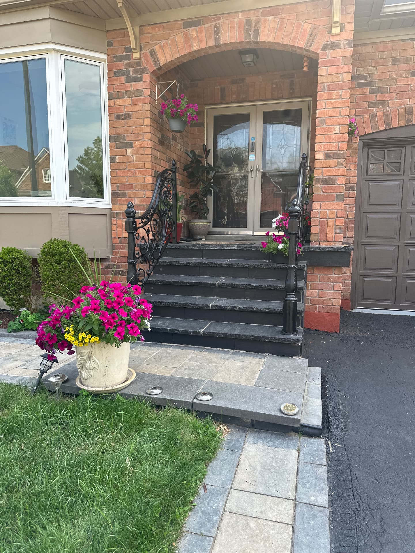 The front entry of a detached home with dark stone steps, black wrought-iron railings, an arched brick entryway and flowering planters