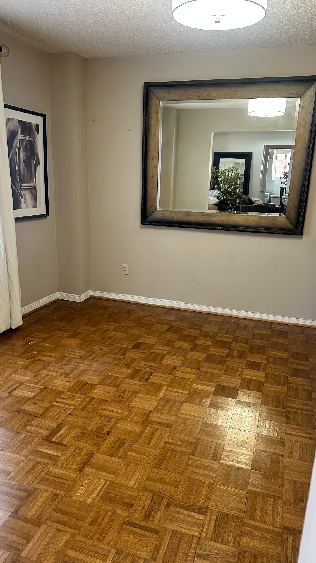 Before the room refresh: an empty living room with parquet flooring, a large wall mirror and horse artwork