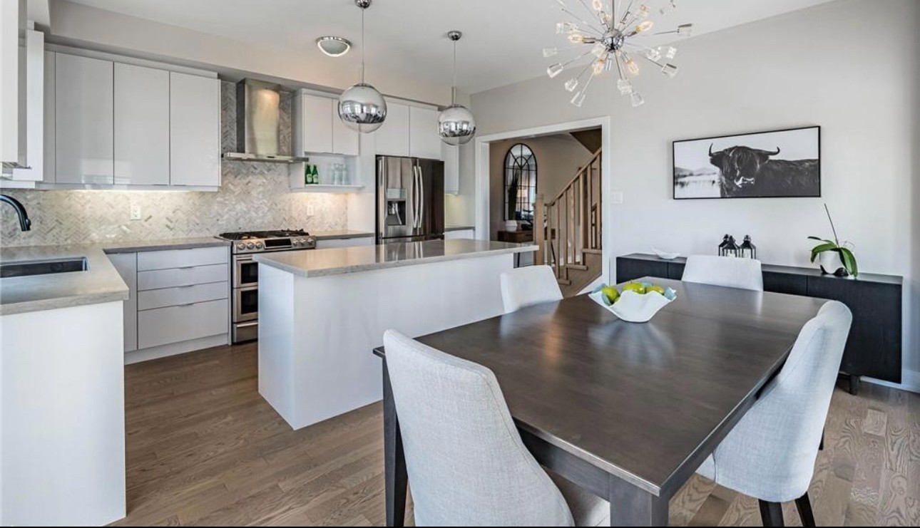 A staged townhouse kitchen and dining area with white cabinetry, a marble backsplash and a dark wood dining table