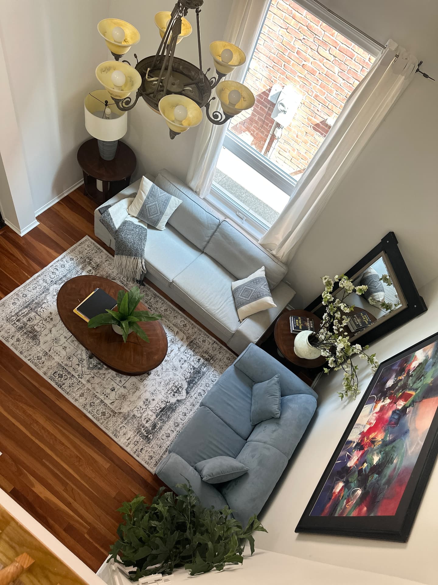 A two-storey living room seen from above, with two sofas, a patterned area rug and a chandelier